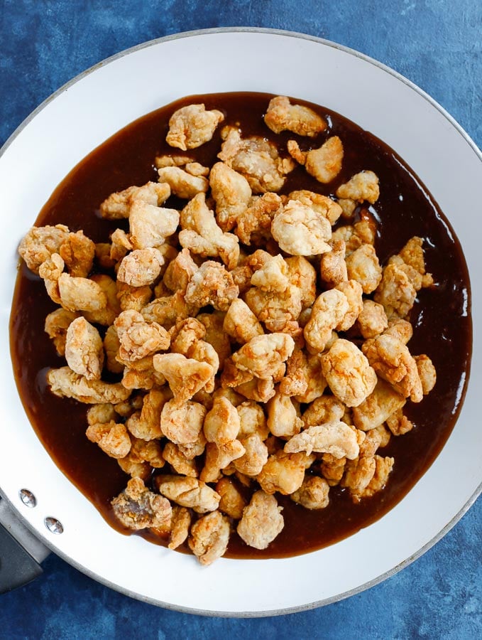 fried chicken bites over the orange chicken sauce in a white skillet before mixing.