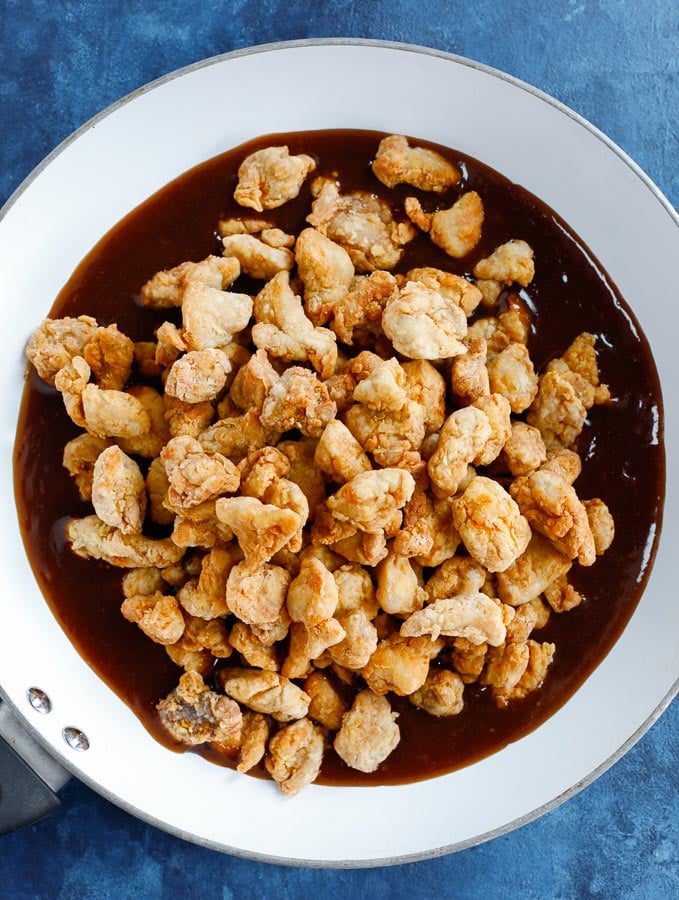 fried chicken bites over the orange chicken sauce in a white skillet before mixing.