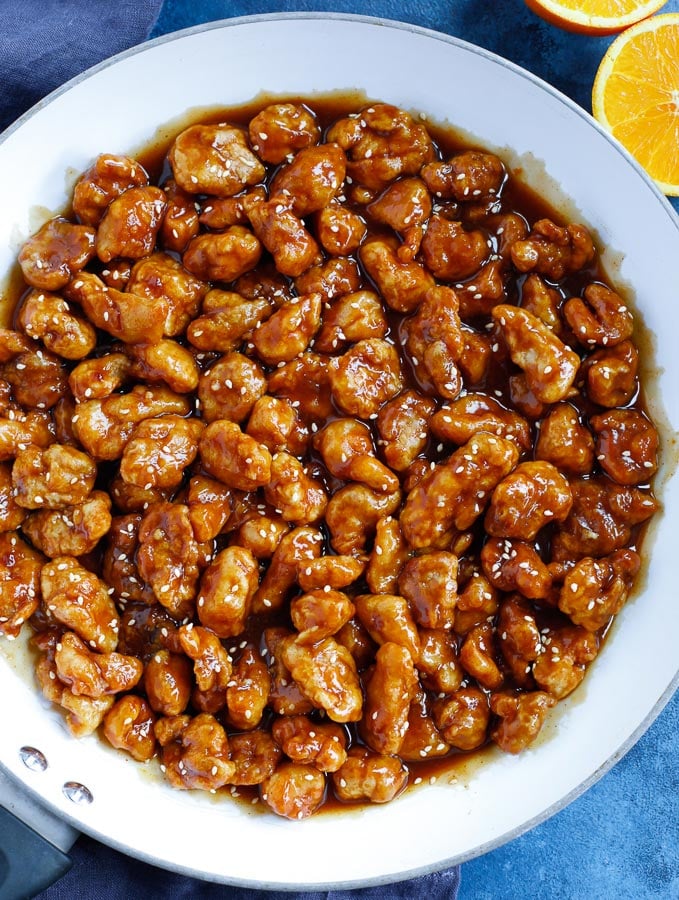 fried chicken bites over the orange chicken sauce in a white skillet after mixing with the sauce.