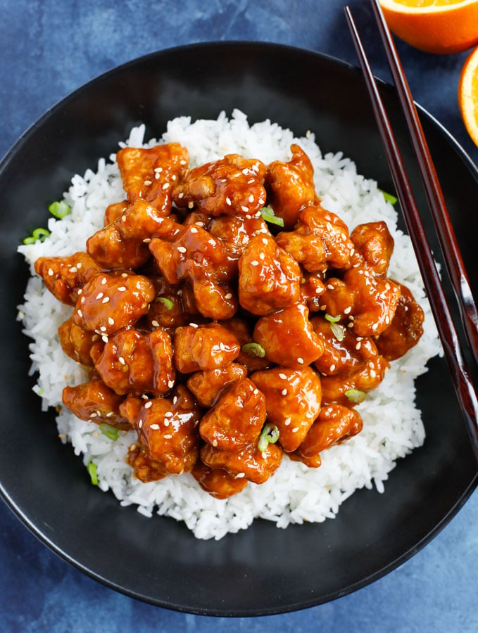 Orange chicken recipe served on a bed of white rice with chop sticks on the side.