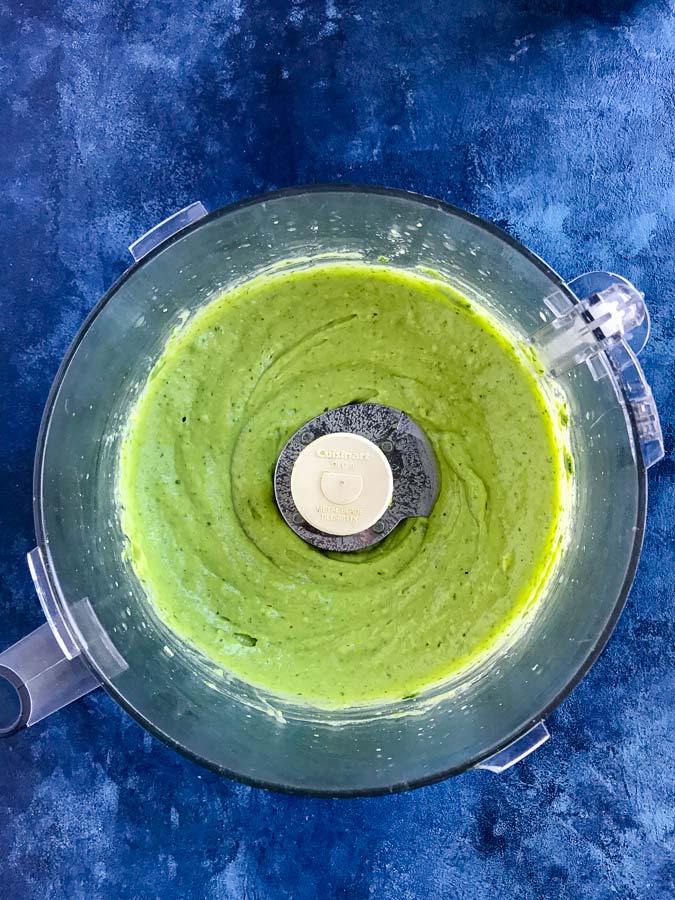 Blender with creamy avocado dressing smoothly blended inside on a blue counter.