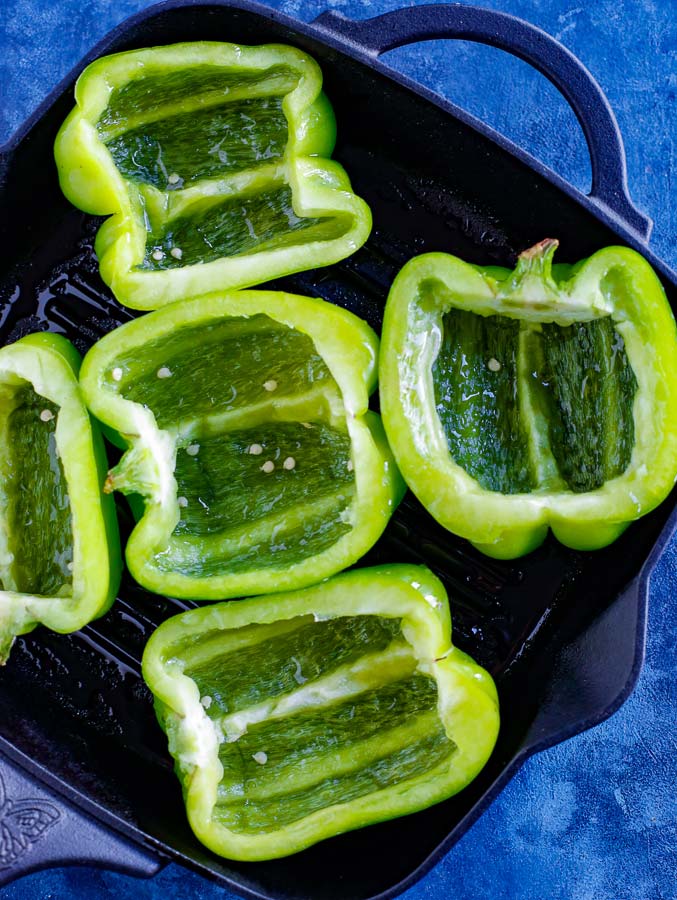 Halved green peppers in a skillet on a blue counter.