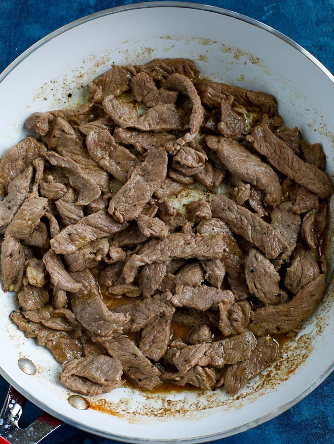 Trimmed steak cooking in a non-stick skillet on a blue counter.