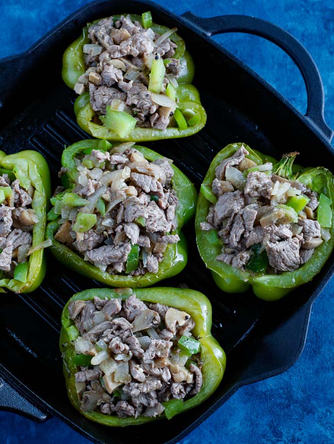 Stuffed bell peppers cooking on a skillet on a blue counter.