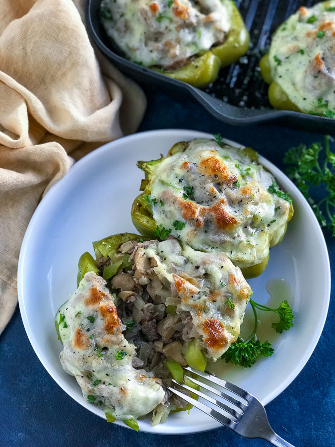 A small white plate with a Philly Cheesesteak Stuffed Bell pepper on a blue counter.