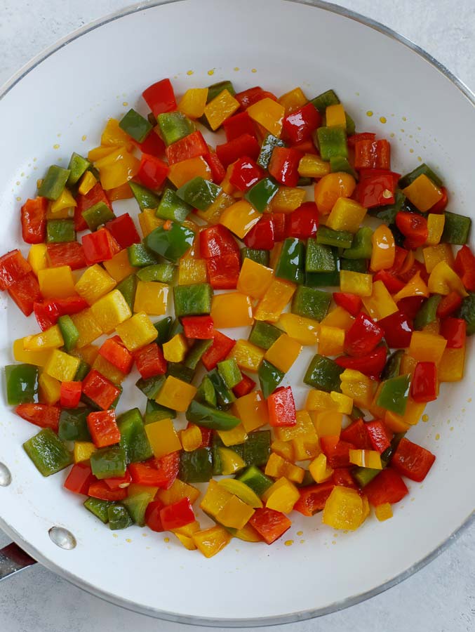 A skillet with red, yellow, and green diced bell peppers cooking.