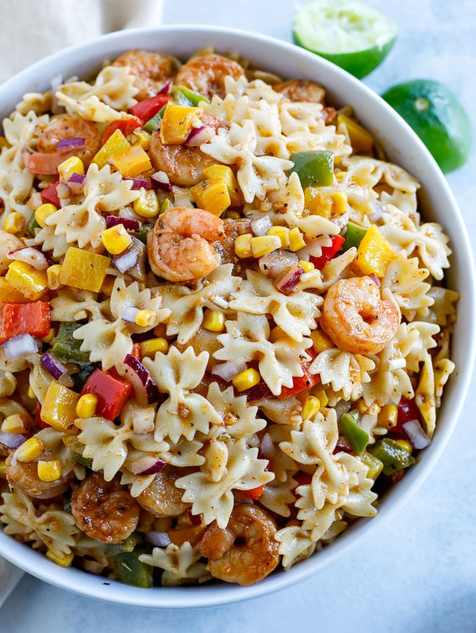 A large white bowl of shrimp fajita pasta salad and two limes in the background.