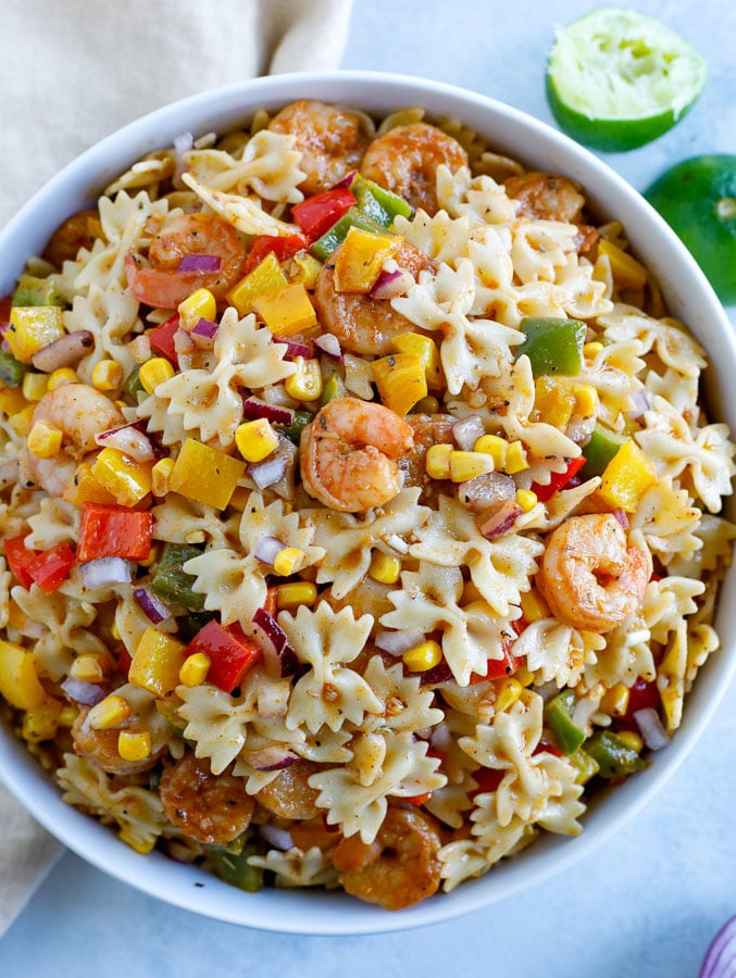 A large white bowl of shrimp fajita pasta salad and two limes in the background.