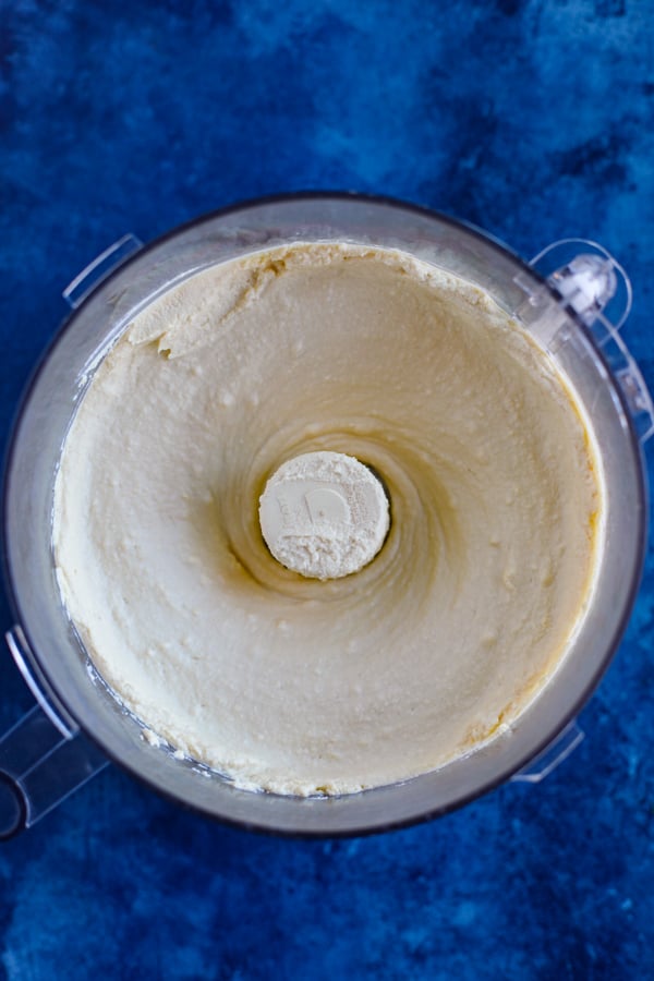 A food processor with fresh hummus on a blue counter.