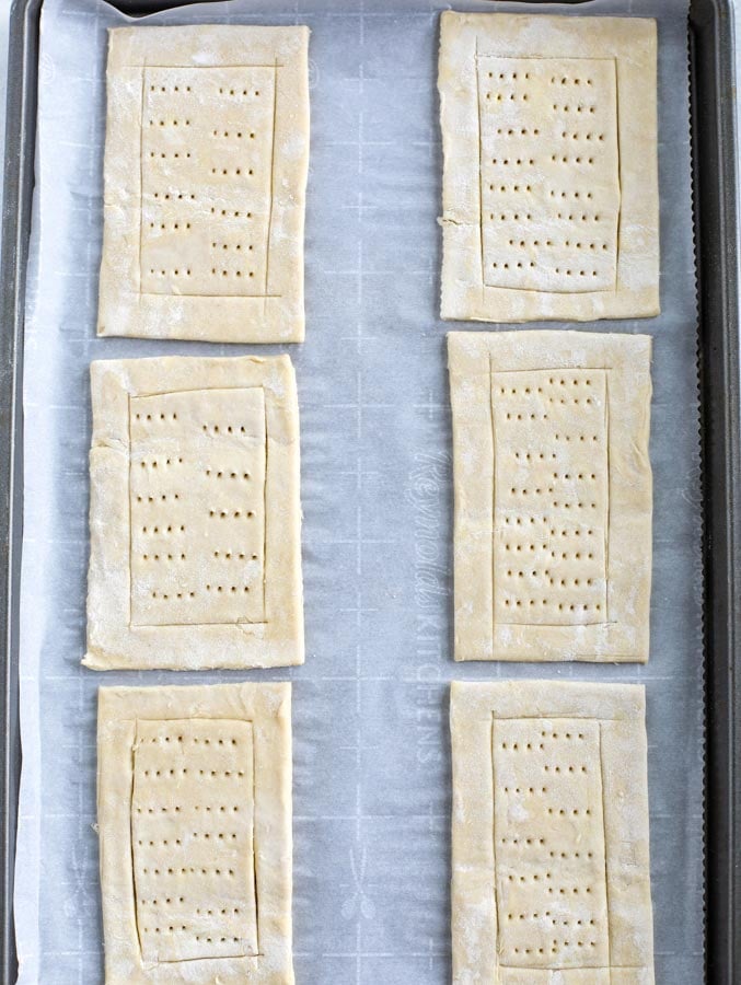 A baking sheet covered with parchment paper with 6 rectangles of puff pastry cut and poked.