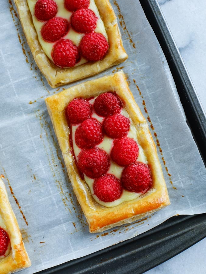 A close up shot of baked raspberry puff pastry rectangles on a parchment paper lined baking sheet.