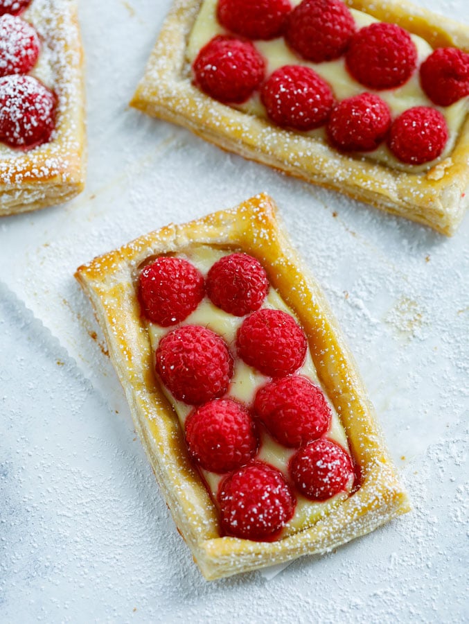 Three raspberry puff pastry tarts on a counter dusted with powdered sugar.