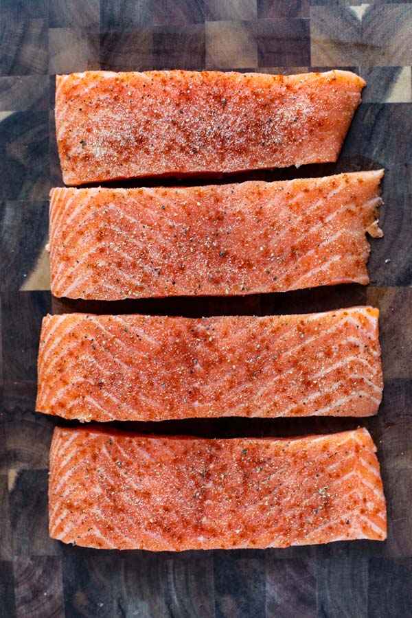 4 raw salmon fillets on a cutting board.