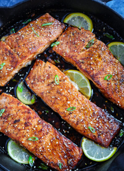 Four spicy honey garlic salmon pieces with lime wedges in a cast ion skillet.