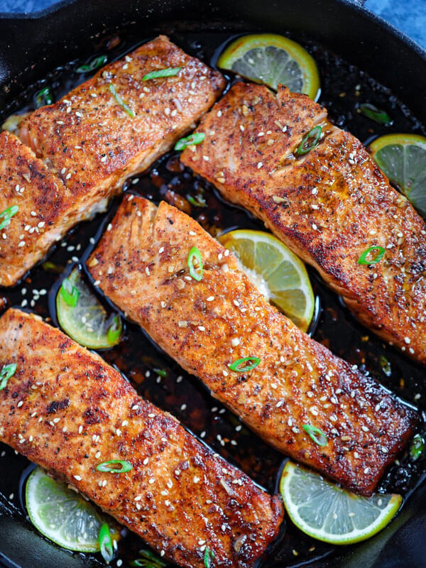 Four spicy honey garlic salmon pieces with lime wedges in a cast ion skillet.