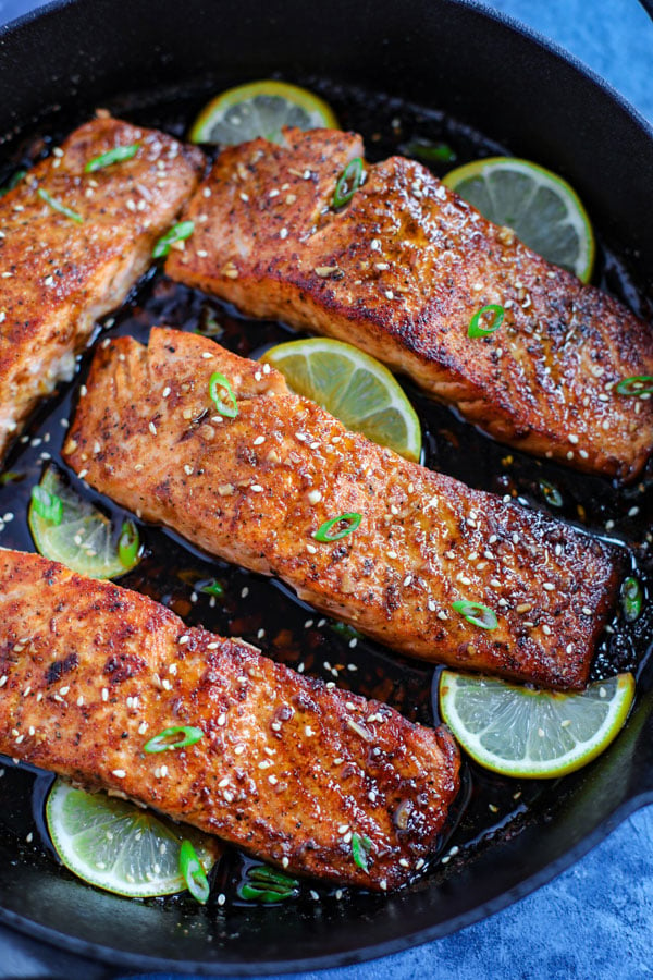 Four spicy honey garlic salmon pieces with lime wedges in a cast ion skillet.