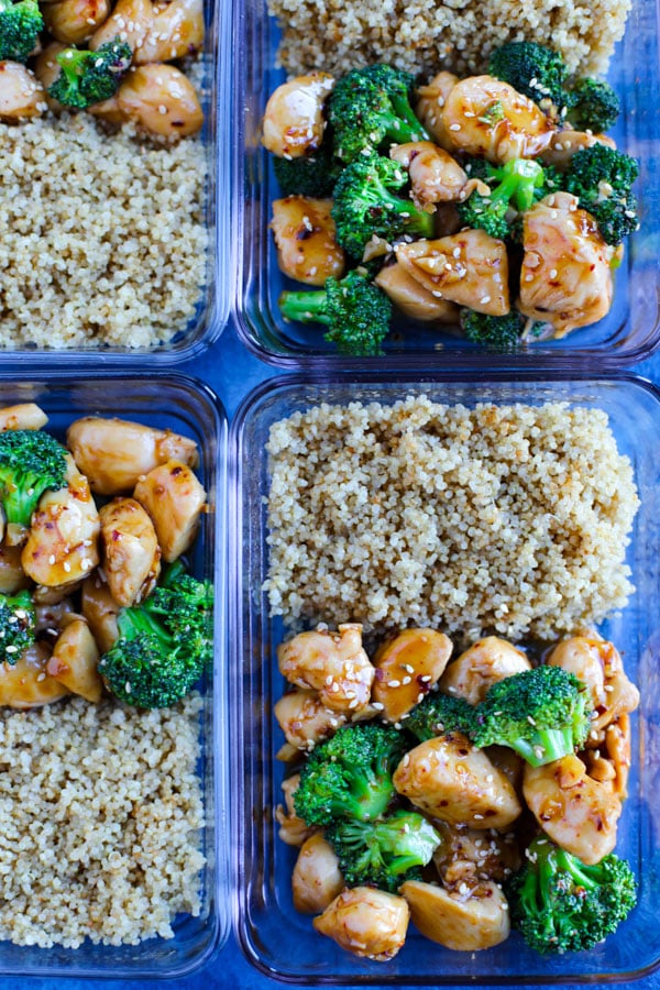 Meal prep containers with Spicy Teriyaki Chicken with Broccoli and brown rice on a blue counter.