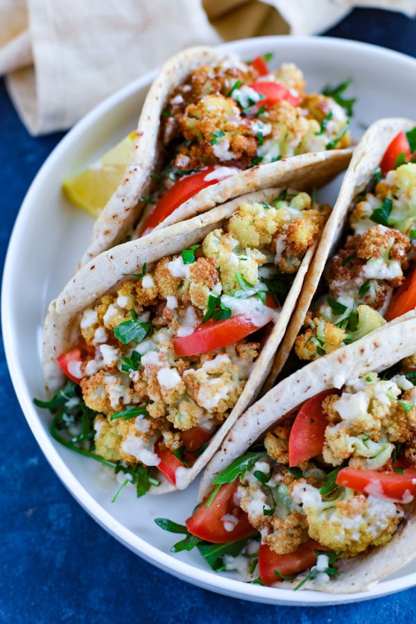 A white plate with 4 vegetarian cauliflower wraps on a blue counter.