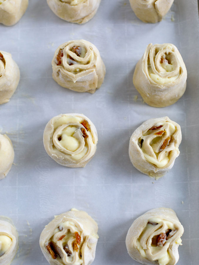 Rolls of pain aux raisins on a parchment paper lined sheet pan.
