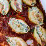 A baking dish with spinach artichoke stuffed shells in tomato basil marinara sauce.