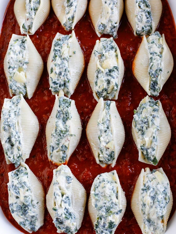 Spinach artichoke stuffed shells lined up in a baking dish.