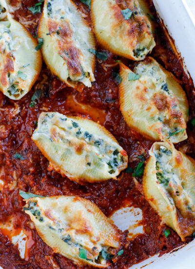 A baking dish with spinach artichoke stuffed shells in tomato basil marinara sauce.