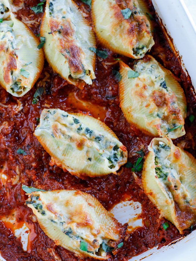 A baking dish with spinach artichoke stuffed shells in tomato basil marinara sauce.