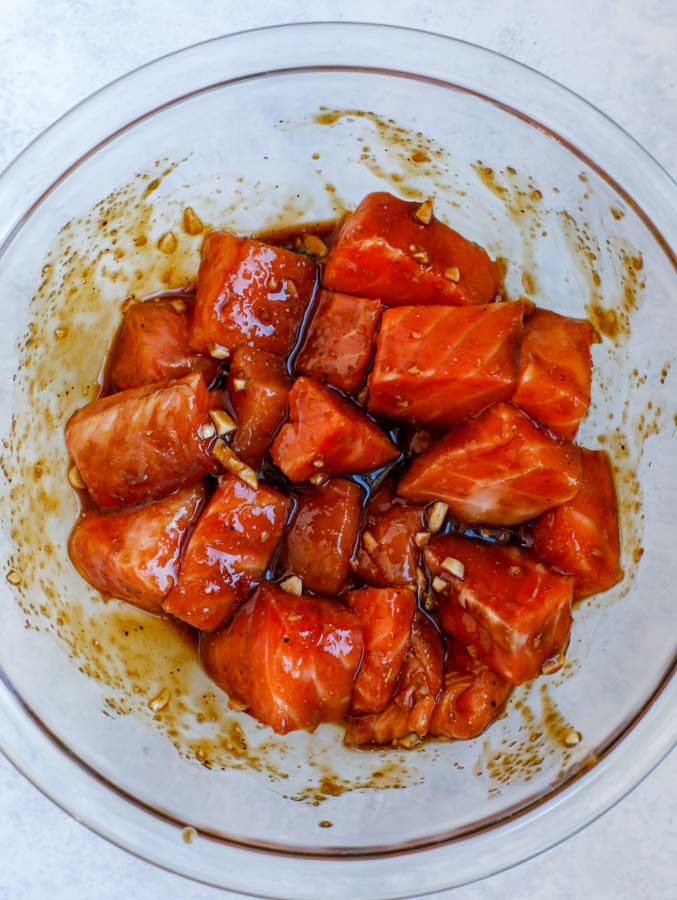 Salmon cubes marinating in a glass bowl of teriyaki sauce.