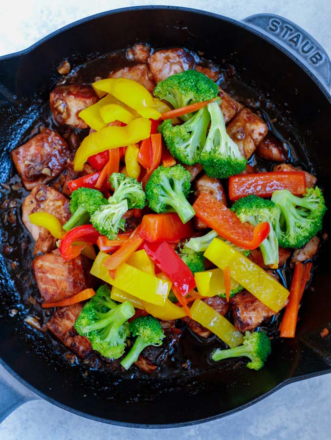 Salmon and stir fry vegetables cooking in a large nonstick skillet.