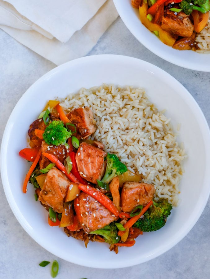 Teriyaki Salmon Stir Fry in a white bowl with rice on a white counter.