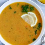 Lebanese lentil soup served in a white bowl and garnished with lemon wedges and parsley
