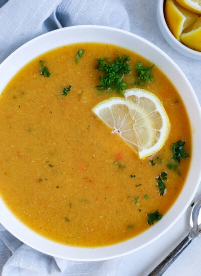 Lebanese lentil soup served in a white bowl and garnished with lemon wedges and parsley