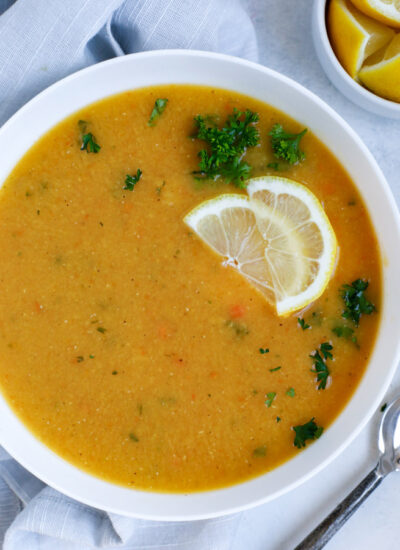 Lebanese lentil soup served in a white bowl and garnished with lemon wedges and parsley