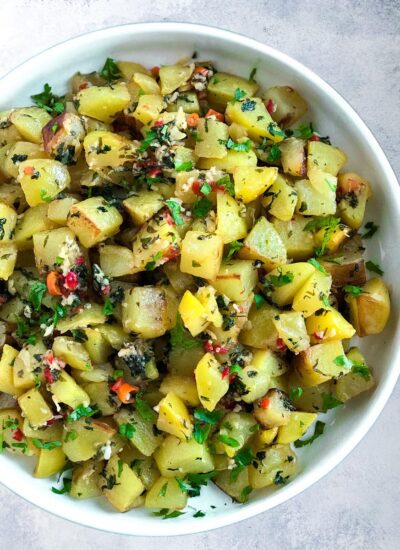 potato cubes friend with cilantro, galic and peppers. served on a plate.