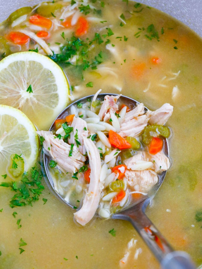A ladle of chicken soup being scooped up form a pot. 
