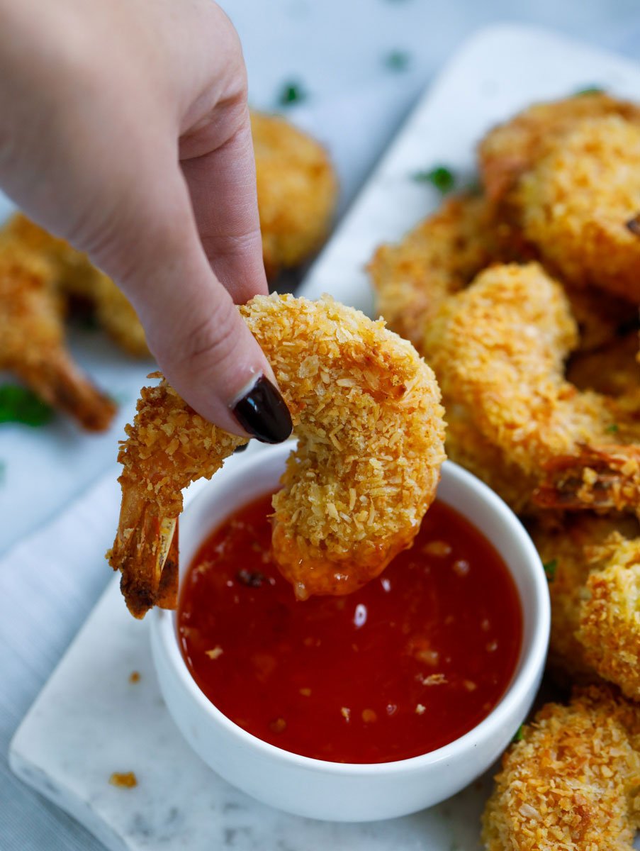 A coconut shrimp being dipped into sweet chili sauce