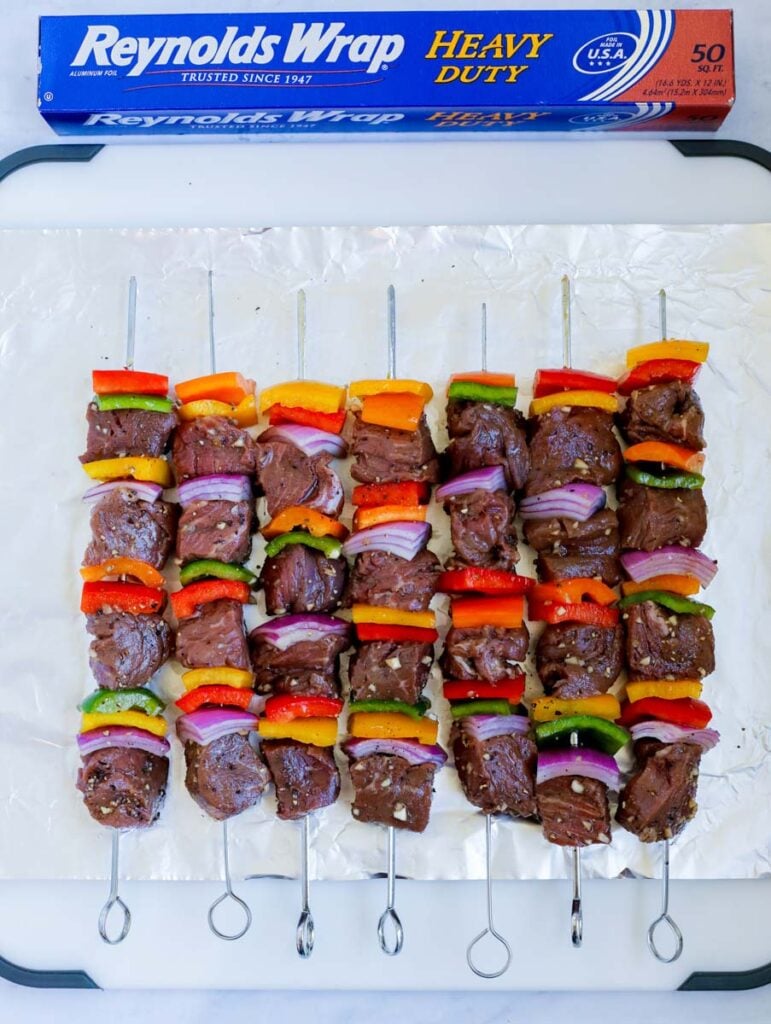 The beef kebobs before grilling laid on foil