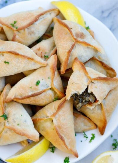 Baked lebanese spinach pies served on a plate with lemon wedges