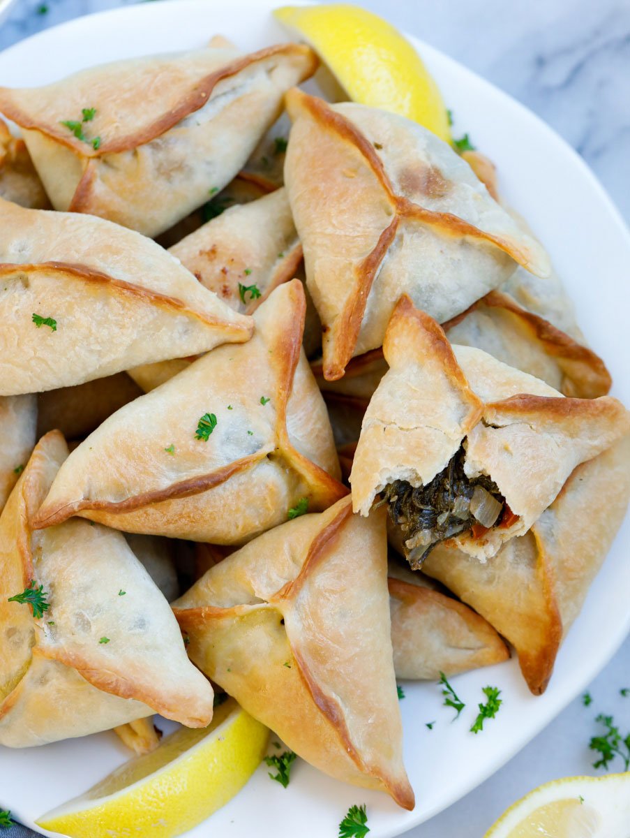 baked Lebanese fatayer spinach pies served on a plate with lemon wedges
