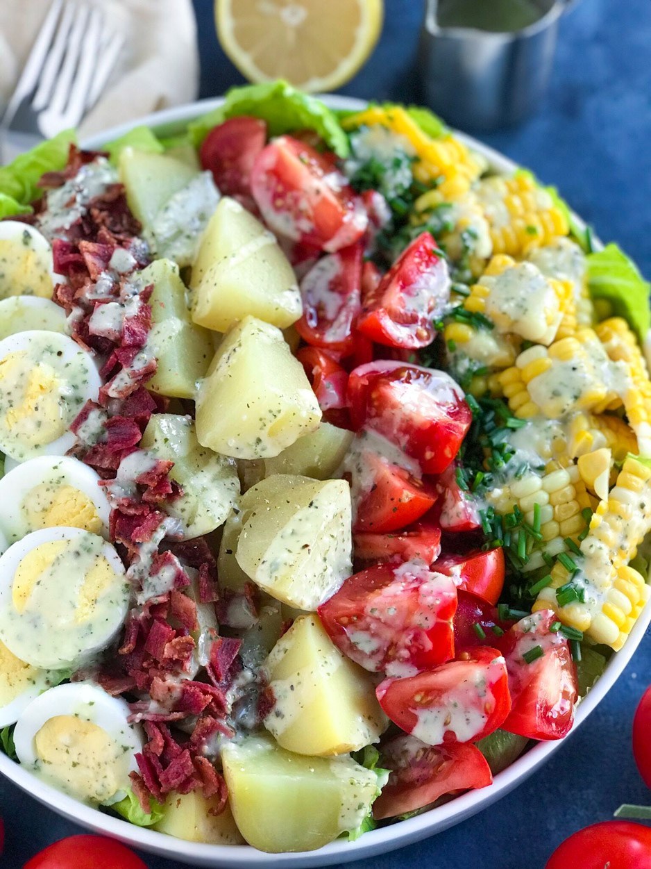 Cobb salad with potatoes, turkey bacon, boiled eggs, tomatoes, chives, corn, dressed in a mayo lemon dressing