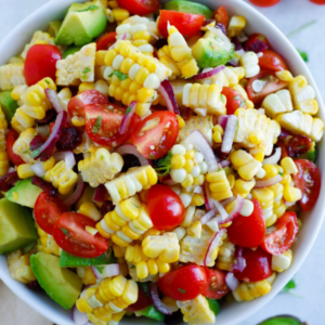Close-up of corn salad with avocado chunks, halved cherry tomatoes, red onion, and dried cranberries.
