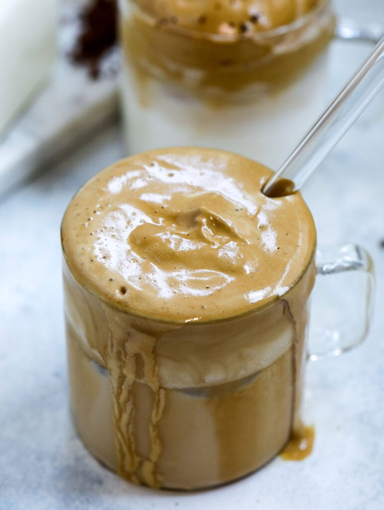 whipped coffee mixed in the milk in a cup with a glass straw