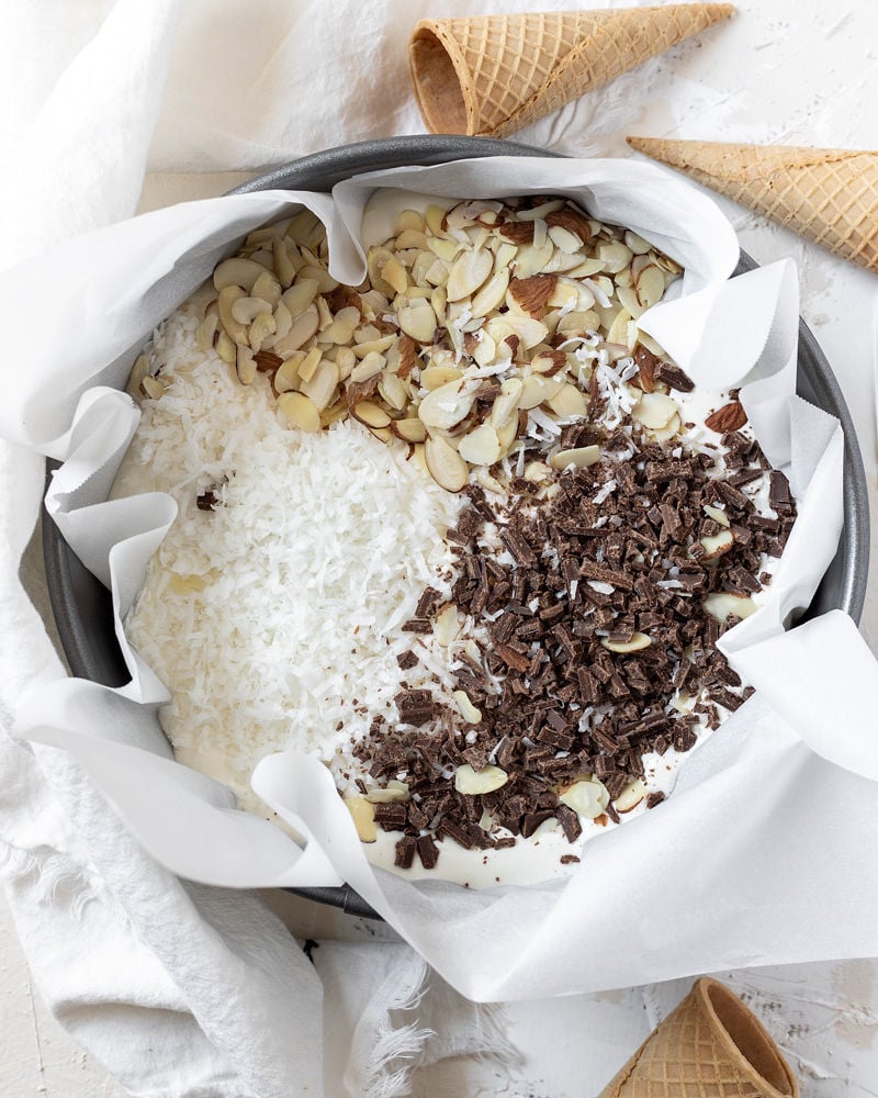 chocolate coconut and almonds in a cake pan on top of the ice cream