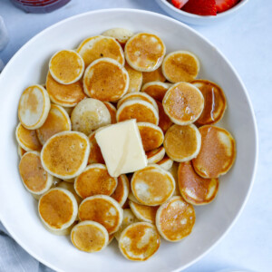 mini pancake cereal served in a bowl with butter and syrup with a side of banana and strawberry fruit