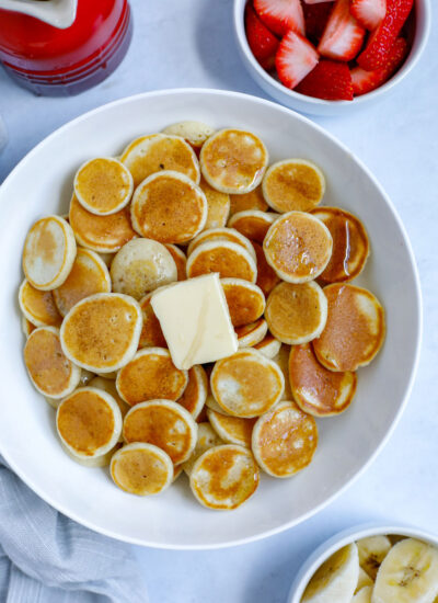 mini pancake cereal served in a bowl with butter and syrup with a side of banana and strawberry fruit