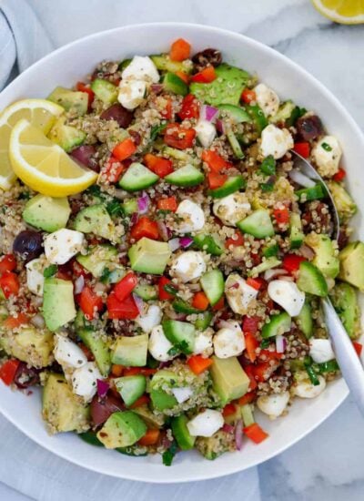 Mediterranean quinoa salad mixed up and served on a dish with a spoon and lemon wedges