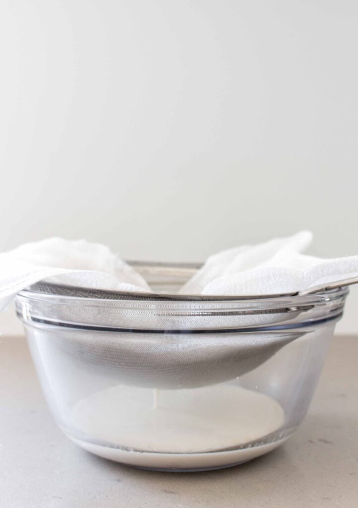 straining almond milk in a strainer and cheesecloth