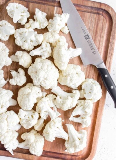 cauliflower cut up on a board with a knife