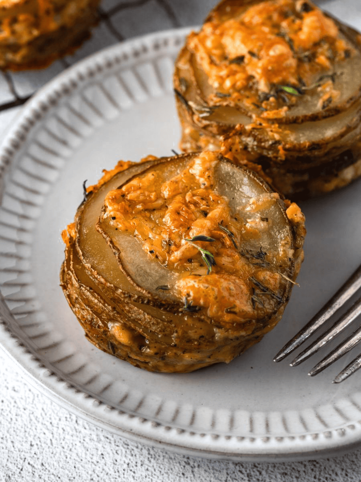 Golden baked potato stacks with melted cheese and herbs served on a plate.