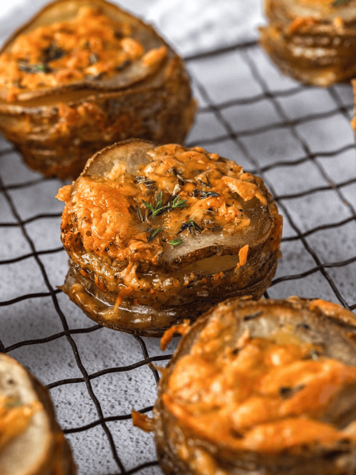 Baked potato stacks topped with melted cheese and fresh herbs on a wire rack.